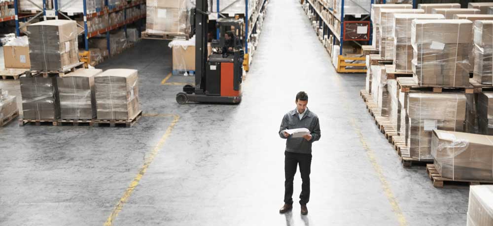 A man reading a paper in the middle of a warehouse.